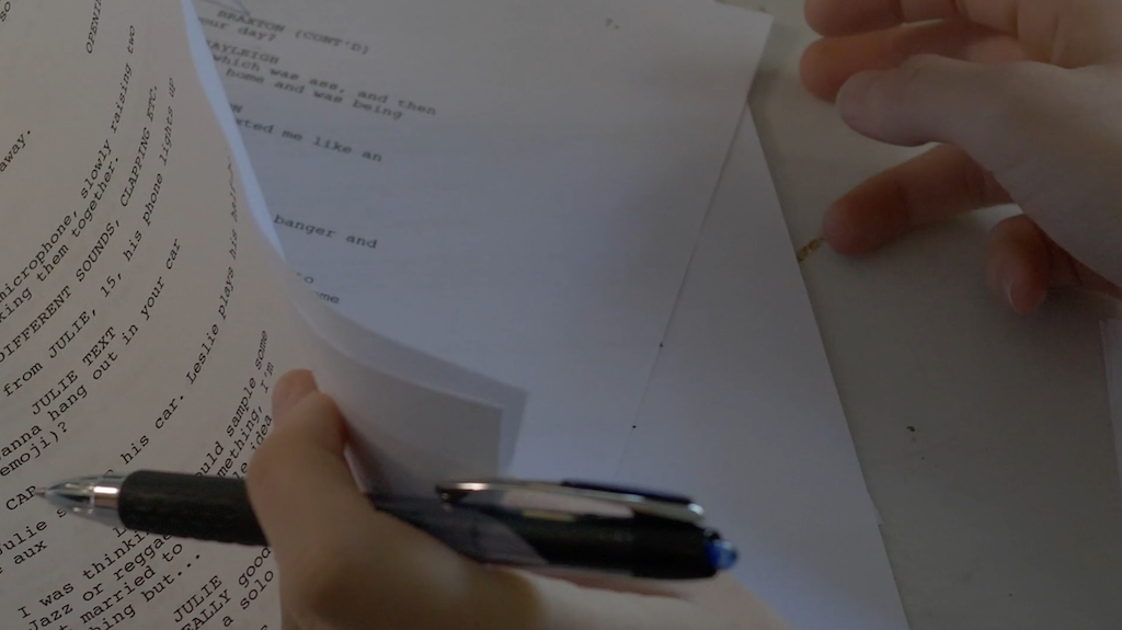 Close-up photo of someone holding a script plus a pen in their left hand